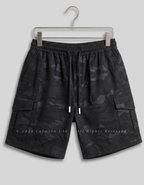 Black camouflage cargo shorts with an elastic drawstring waist, hanging on a metal hanger against a light gray background.