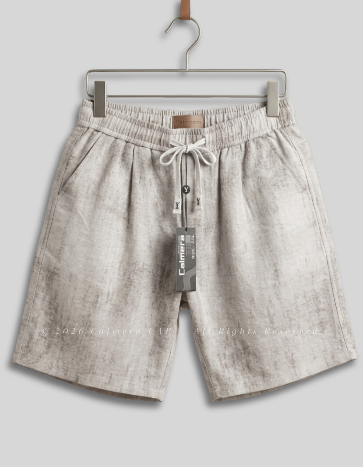 A pair of light beige linen drawstring shorts hanging on a metal hanger against a solid gray background. The shorts feature a textured, slightly mottled linen pattern, an elastic waistband, and a white drawstring.