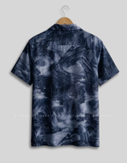 A short-sleeve camp collar shirt with an all-over dark blue and gray landscape print, shown hanging on a wooden hanger against a light gray background.