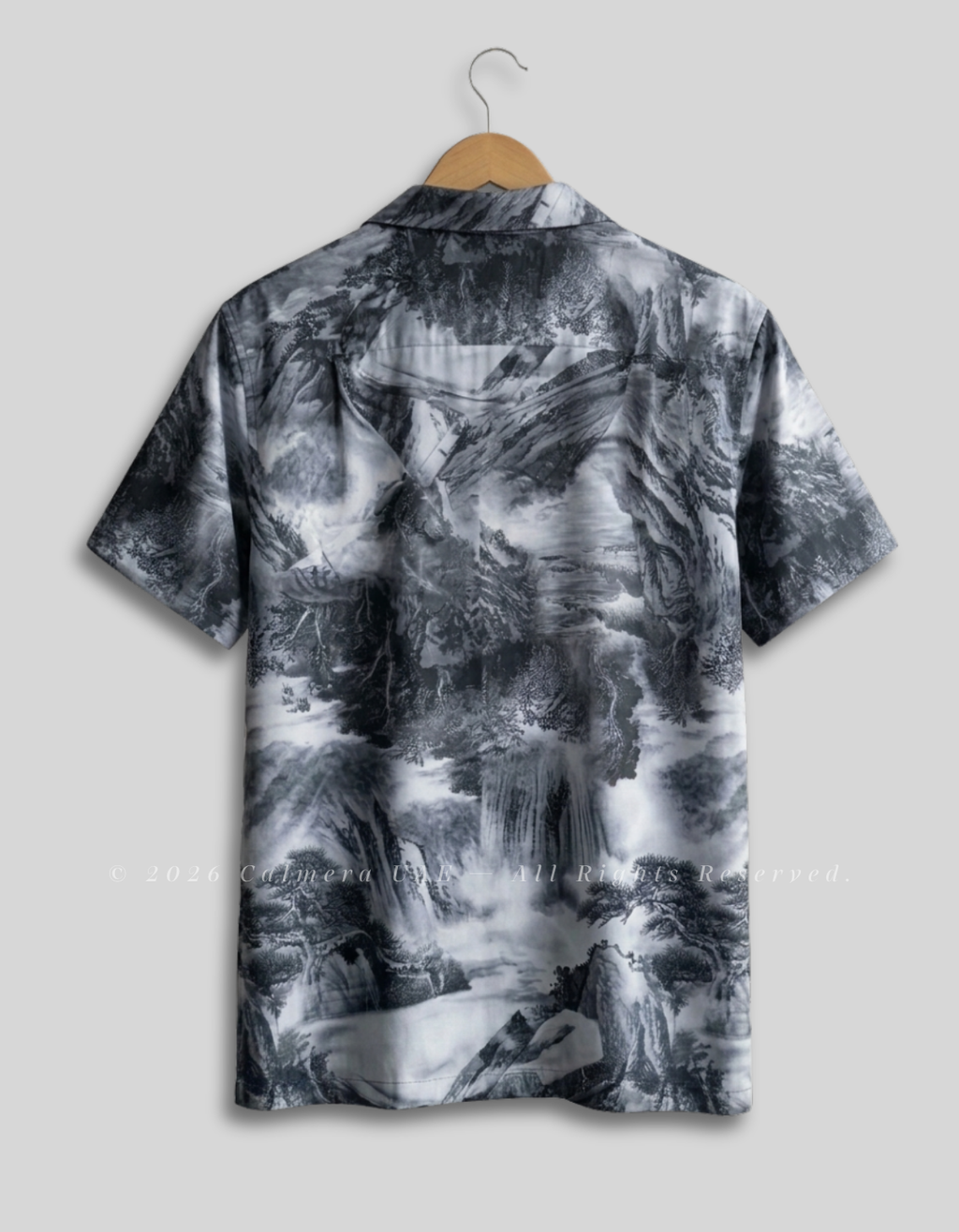 A short-sleeve camp collar button-up shirt with an all-over black, gray, and white misty mountain landscape print, hanging on a wooden hanger against a light gray background.