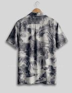 A short-sleeve button-up shirt hanging on a wooden hanger against a light gray background. The shirt features a monochrome, painterly landscape print with black, gray, and white tones depicting mountains, waterfalls, and mist.