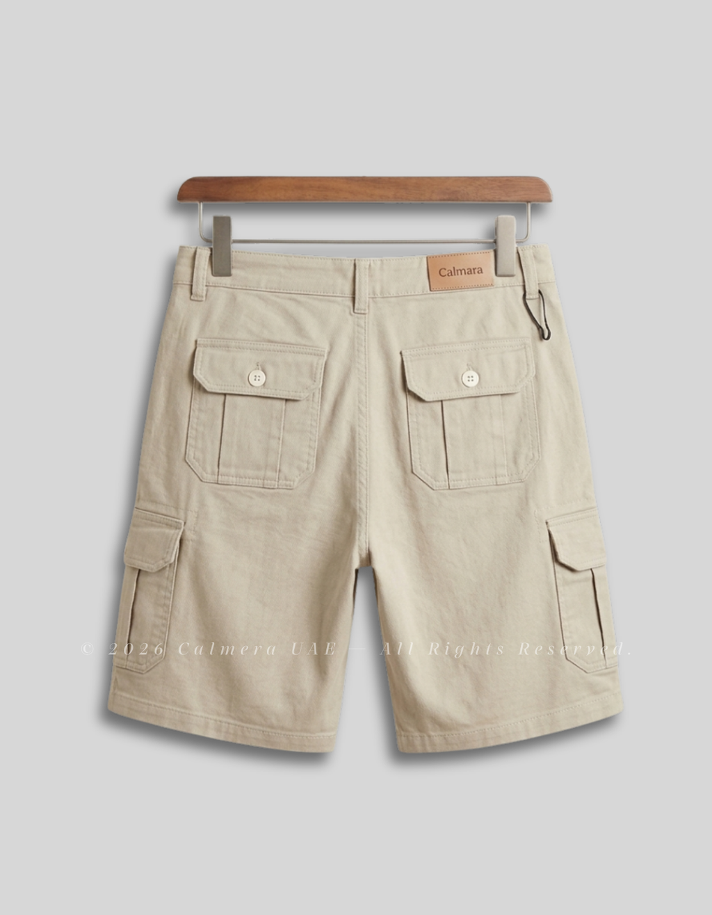 Beige cargo shorts with flap pockets, shown from the back on a wooden hanger against a light gray background.