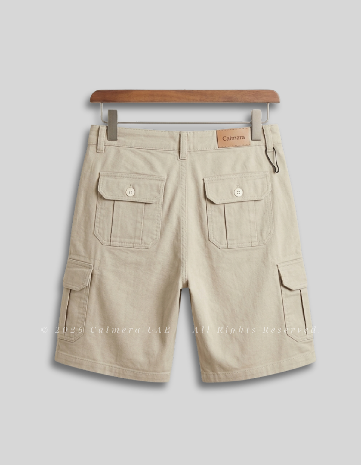 Beige cargo shorts with flap pockets, shown from the back on a wooden hanger against a light gray background.