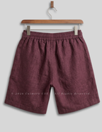 A pair of men's casual shorts in a textured burgundy fabric, hanging from a wooden hanger against a light gray background.
